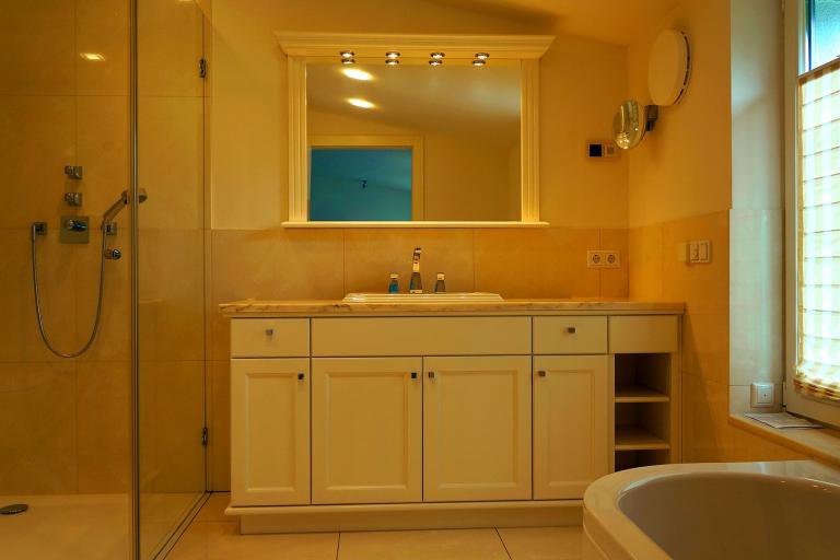 Badezimmer mit Waschtisch mit weißen Fronten und Spiegel mit Holzrahmen